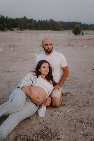 Intimate maternity photoshoot on a sandy beach showing couple relaxing together.