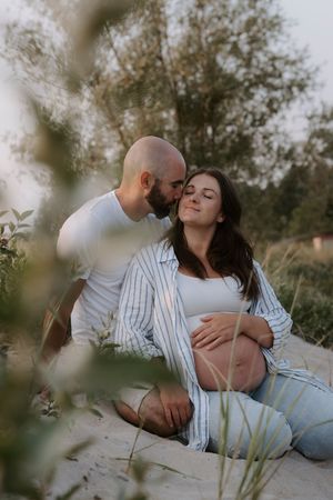 An intimate maternity portrait of a couple sitting among beach grass at sunset.