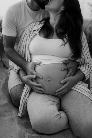 Black and white intimate maternity photos showing a pregnant belly with hands gently resting on it.