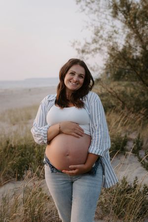 Outdoor maternity photos in a field showing a pregnant woman in striped shirt and jeans.