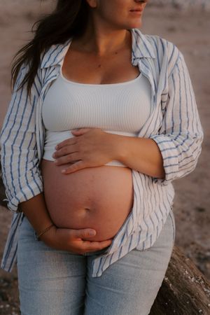 Close-up maternity photos showing pregnant belly with striped shirt and jeans against beach backdrop.