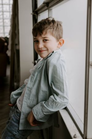 Natural light portrait showing person in denim and light blue button-up shirt by window.