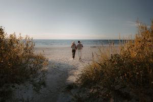 Distant figures walk along a serene beach landscape at sunset.