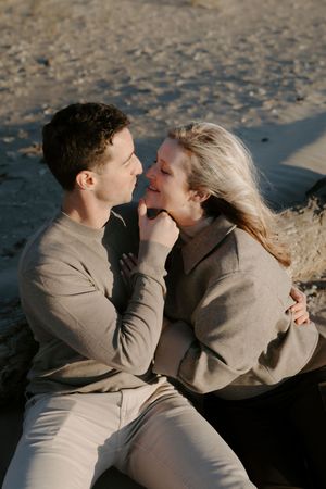 Couple in matching beige sweaters sharing intimate moments on sandy beach.