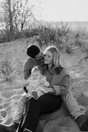 Black and white photo of a family moment on sandy dunes with a baby.