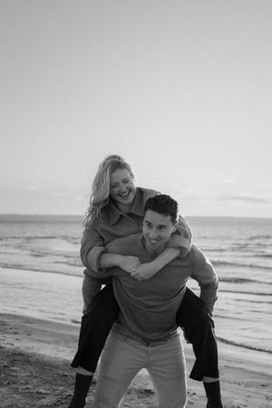 Playful piggyback ride moment captured in black and white on beach.