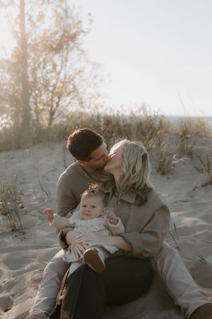A family shares tender moments together on sandy dunes during golden hour.