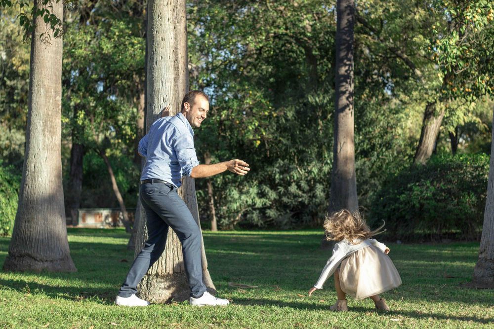 Parent and child playing together in a sunny park with trees.