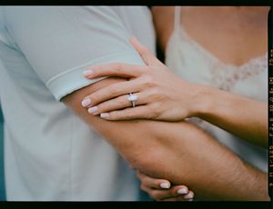 Close-up photo of hands with engagement ring showing wedding proposal moment against soft neutral background.
