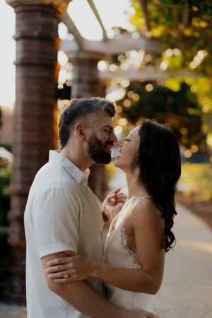 Couple embracing in golden sunlight beneath pillars during a romantic photoshoot.
