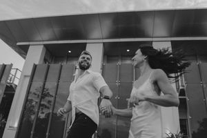 A couple dances together in black and white photography outside a modern building.