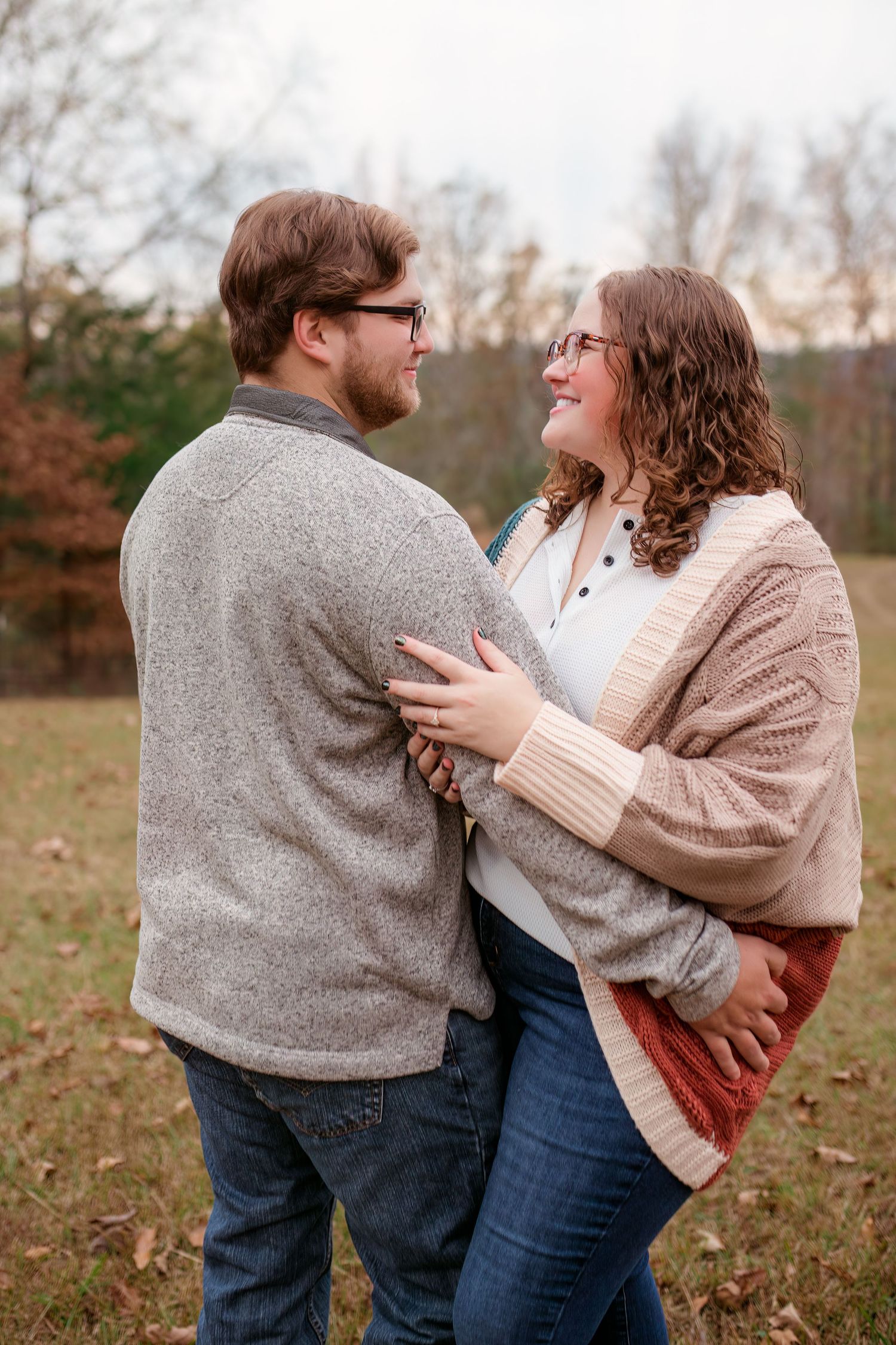 Couple embracing and laughing together outdoors wearing cozy sweaters on an autumn day.
