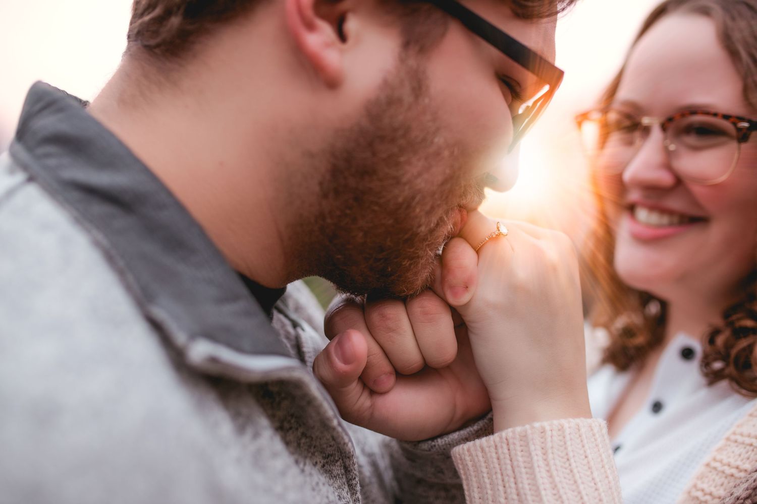 Intimate moment between couple as one kisses the other's hand during golden hour.