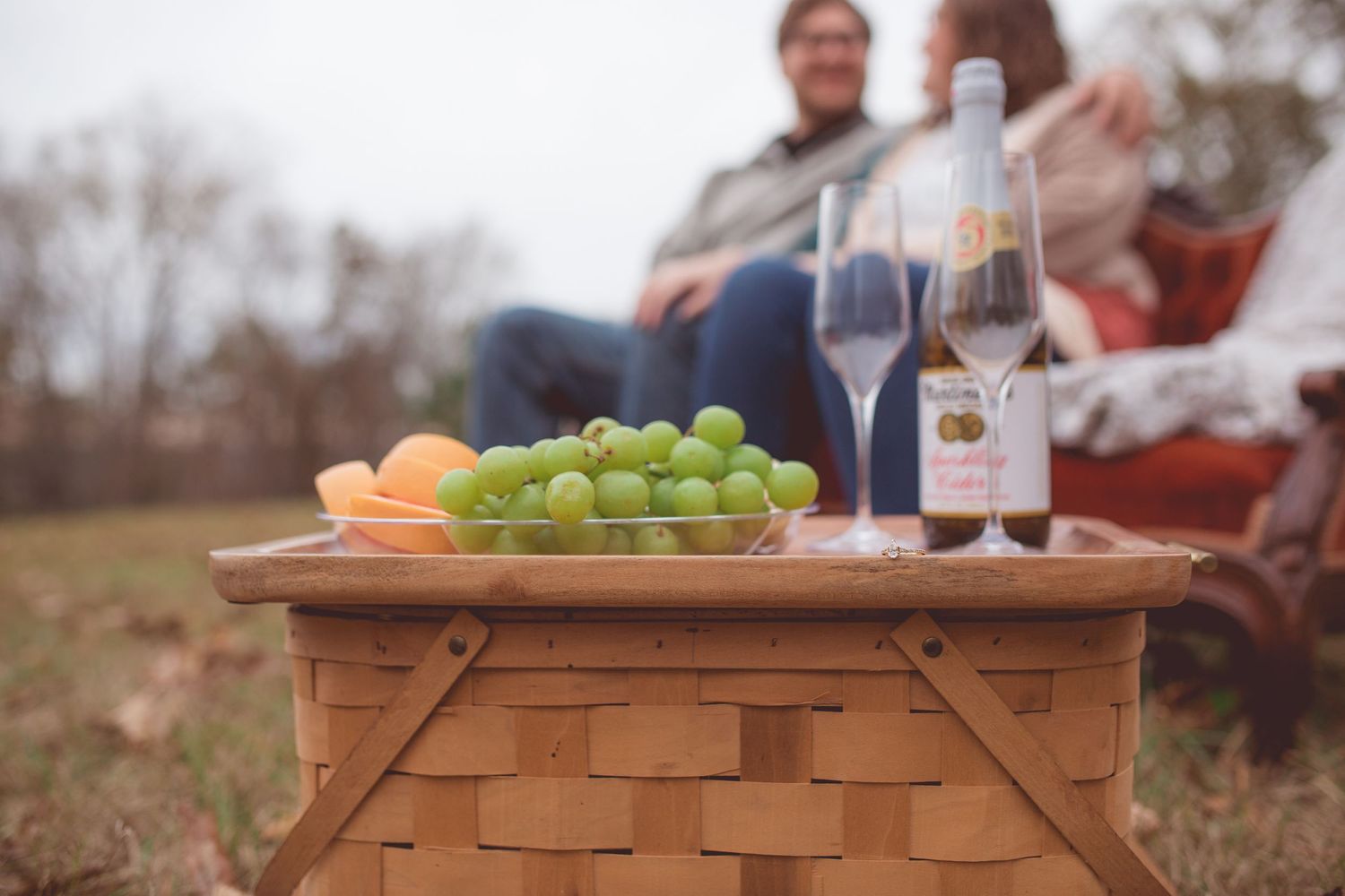 Picnic setup with wine glasses, grapes and oranges on wooden basket outdoors.