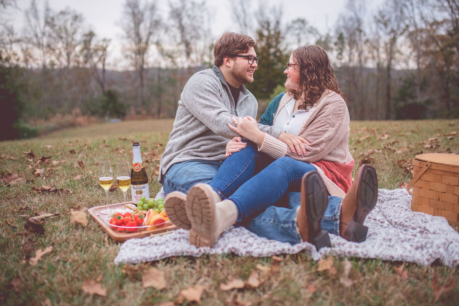 Couple enjoying romantic picnic on blanket outdoors with wine and snacks.