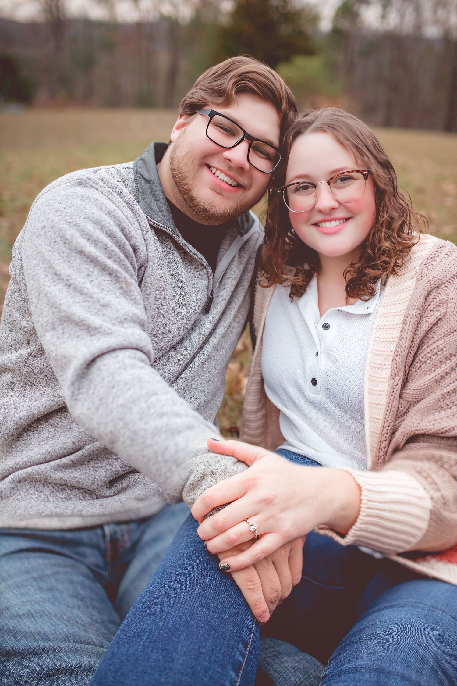 A cozy outdoor portrait of a couple in sweaters sitting close together on an autumn day.