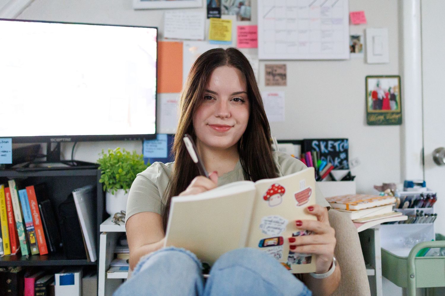 Woman in light blue off-shoulder top holds black book while looking up thoughtfully.