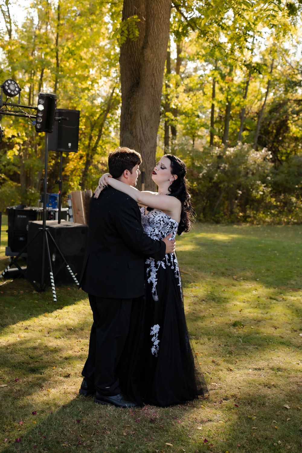 Wedding couple in black attire sharing intimate moments in a sunlit garden setting.