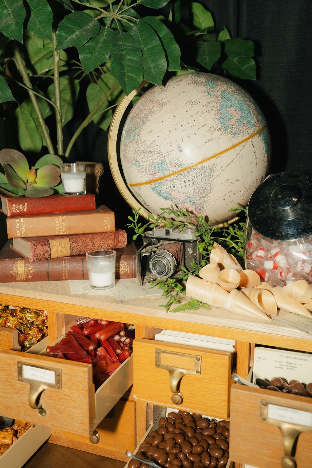 Vintage candy buffet with globe, old books, camera, and wooden card catalog drawers filled with assorted sweets.