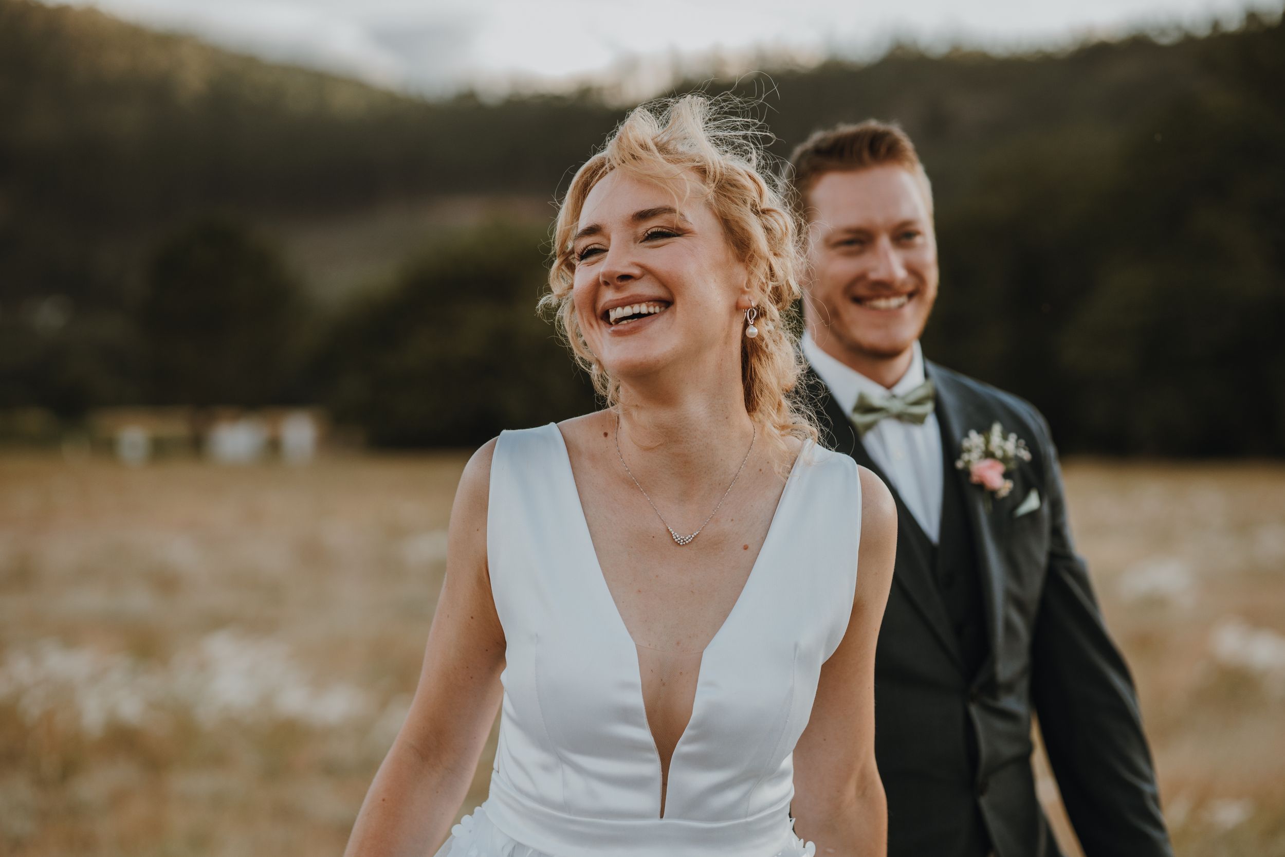 A joyful wedding couple laughs together in a sunlit field during golden hour.