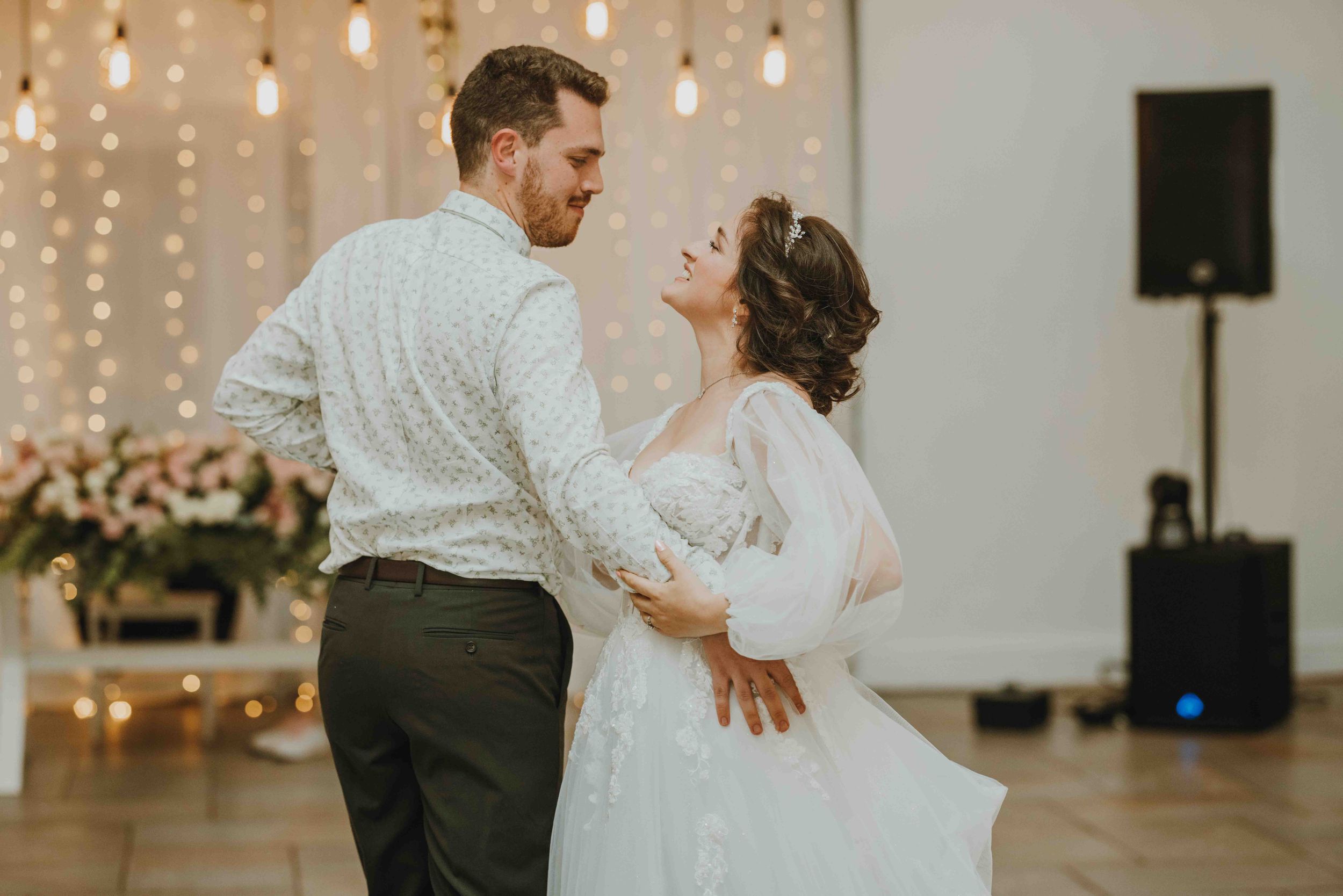 A bride and groom share their first dance surrounded by warm fairy lights at a romantic wedding reception.
