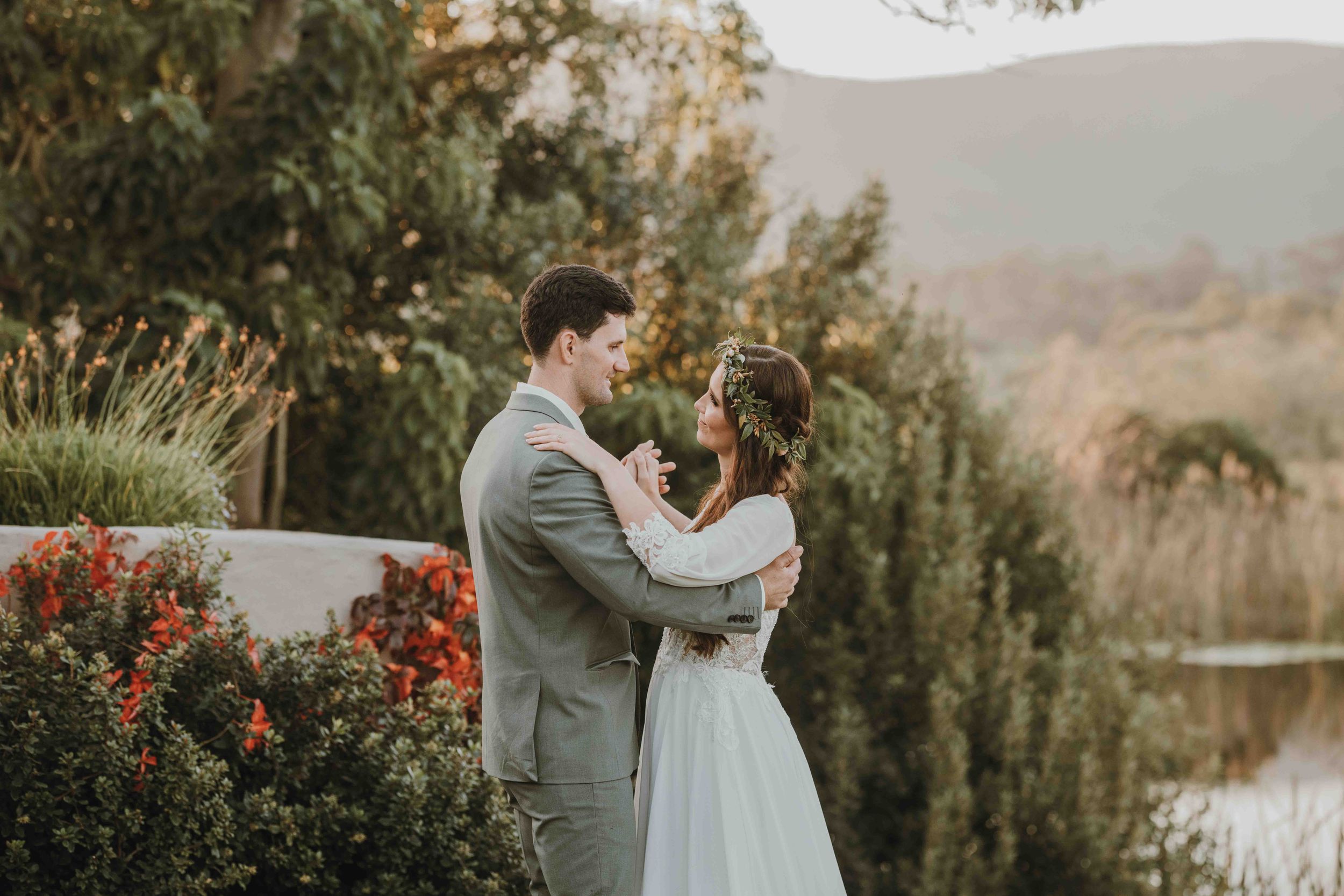 Bride and groom share a romantic moment outdoors with lush greenery and mountain views at their wedding.