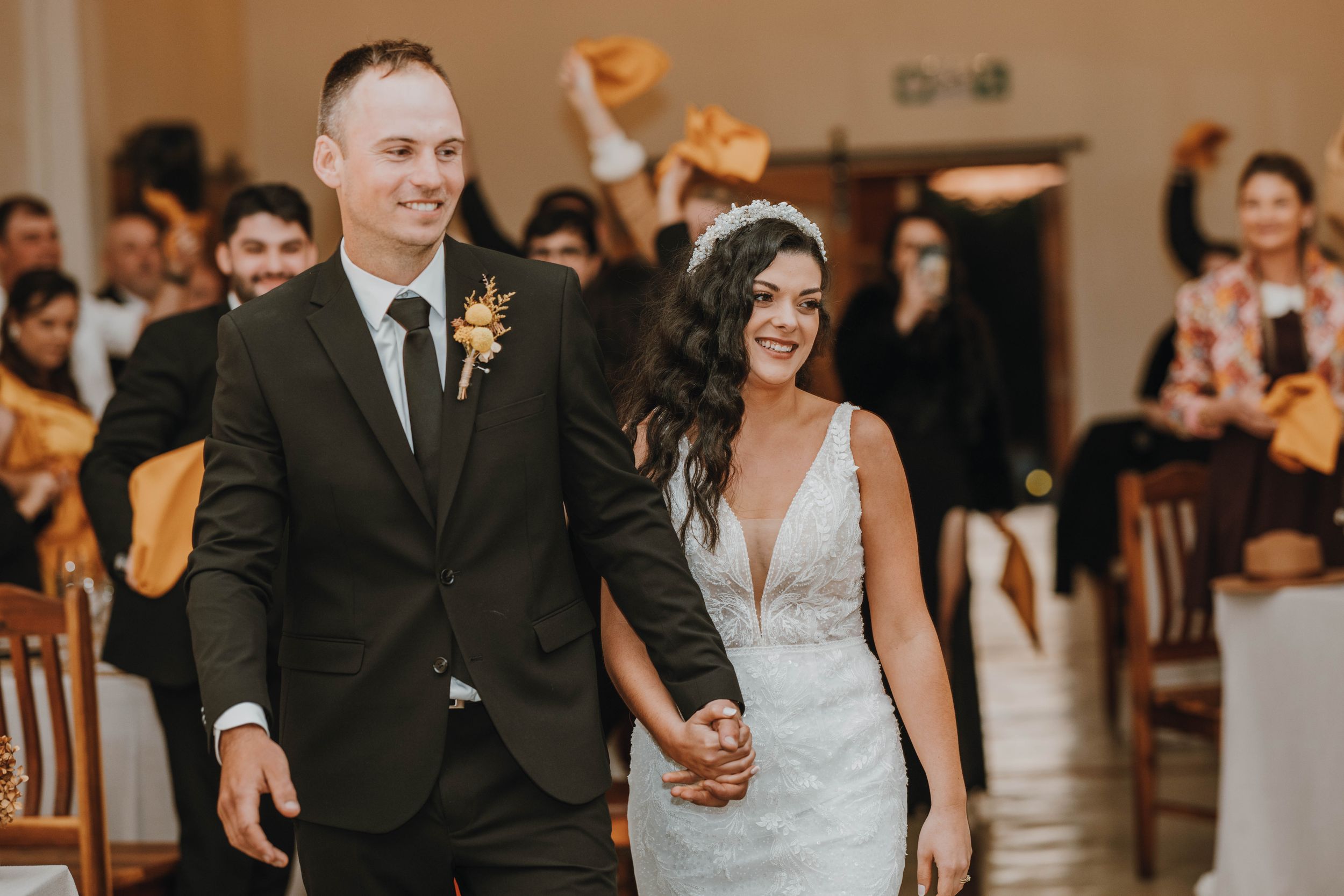 Wedding guests dance and celebrate on a wooden dance floor at an indoor reception venue.