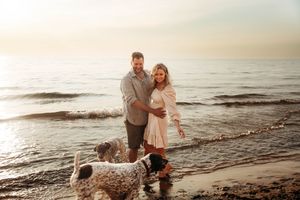 Couple smiling with two dogs at the beach during golden hour sunset.
