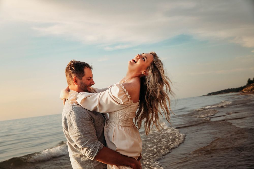 Joyful couple laughing and embracing on a beach at sunset.