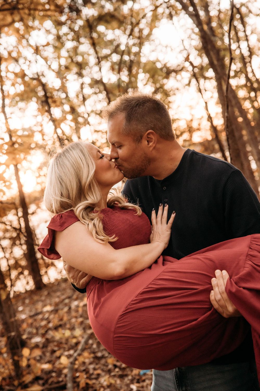 Man carrying woman in his arms for a romantic kiss in autumn forest.
