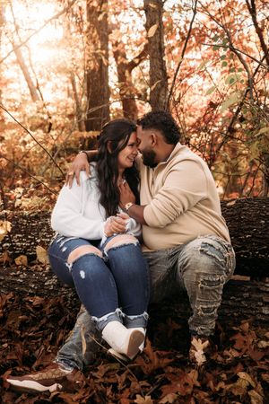 Couple sitting on a log sharing a romantic moment surrounded by colorful autumn leaves.