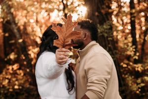 Couple hiding behind a large autumn oak leaf for a playful kiss in the forest.