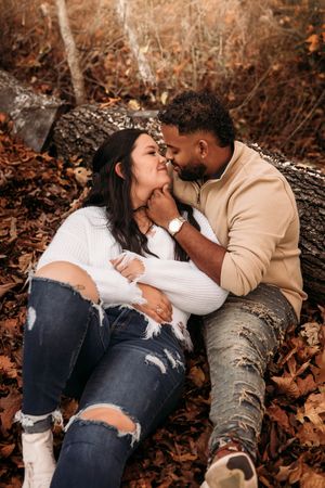 Couple sharing an intimate moment lying against a log surrounded by fall leaves.