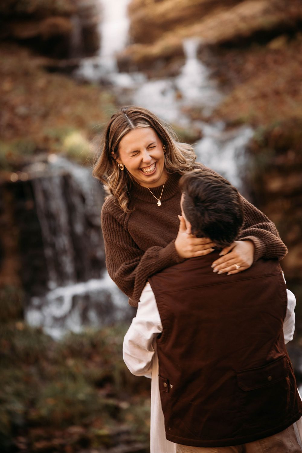 Laughing woman embracing man in front of a beautiful waterfall backdrop.