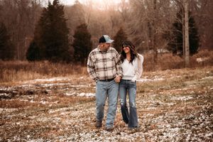 Romantic couple holding hands while walking through a snow-dusted field during golden hour.