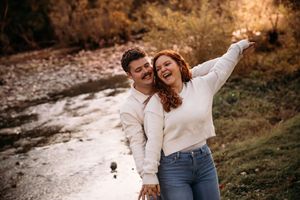 Happy couple laughing and embracing outdoors near a creek in fall.
