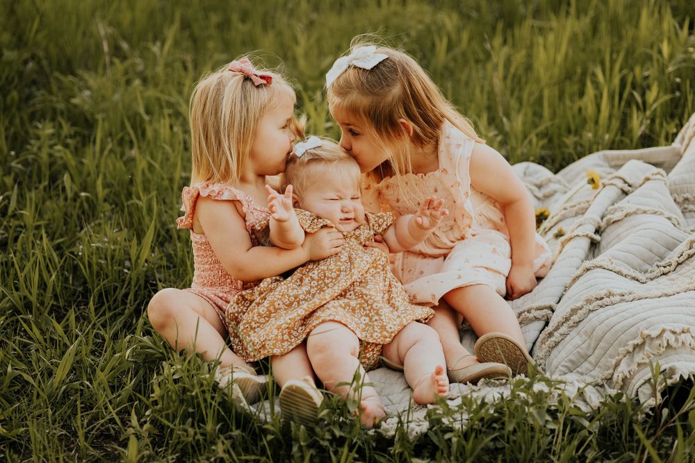 Two small children in floral dresses sitting together on a blanket outdoors during golden hour.