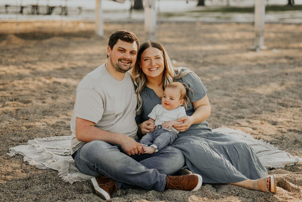 Family sitting on blanket during outdoor photo session in rustic setting.