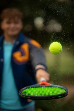 Tennis ball floating above a green racket in an artistic action shot.