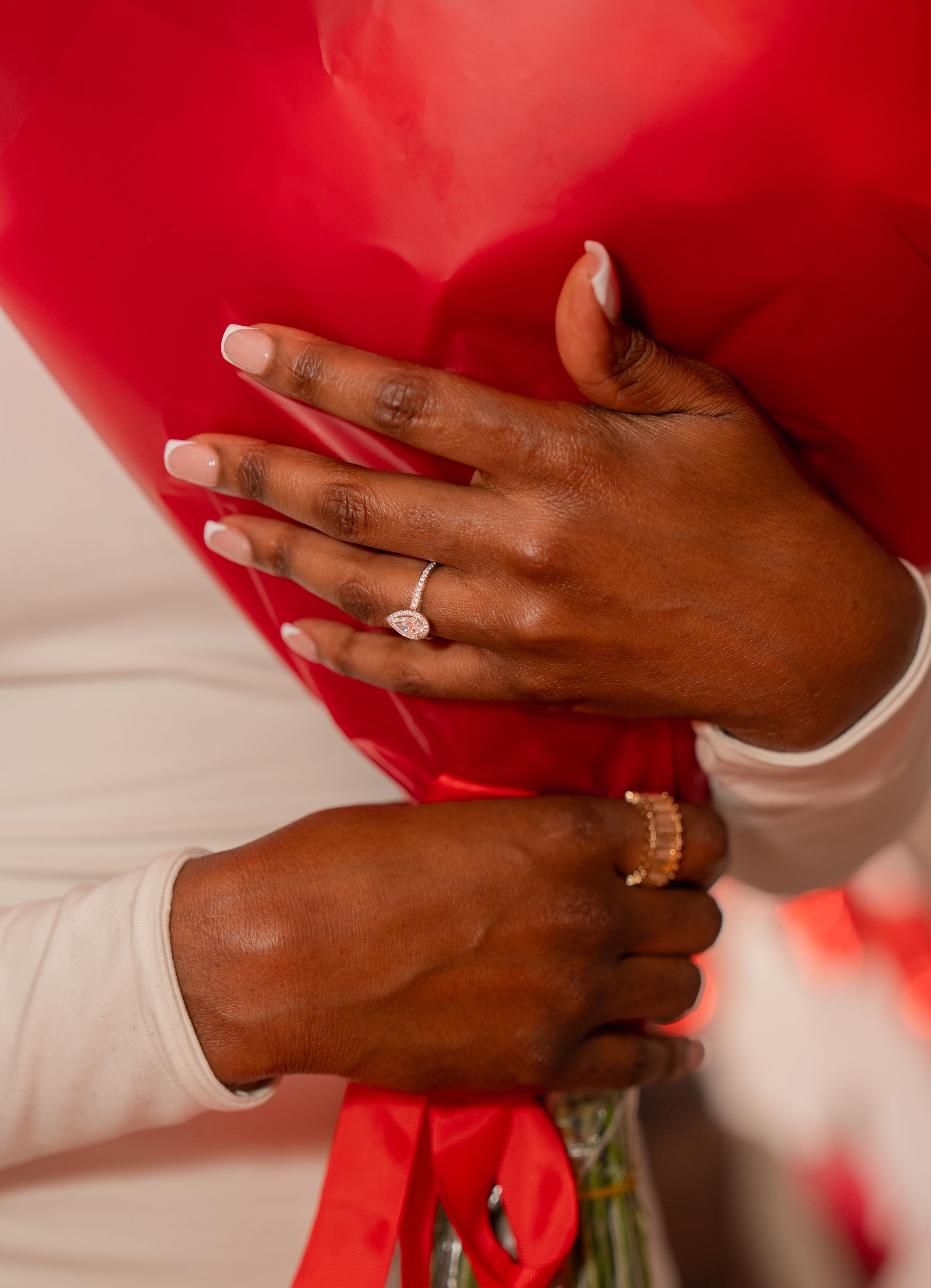 Close-up of hands wearing engagement and wedding rings against a red and white background.