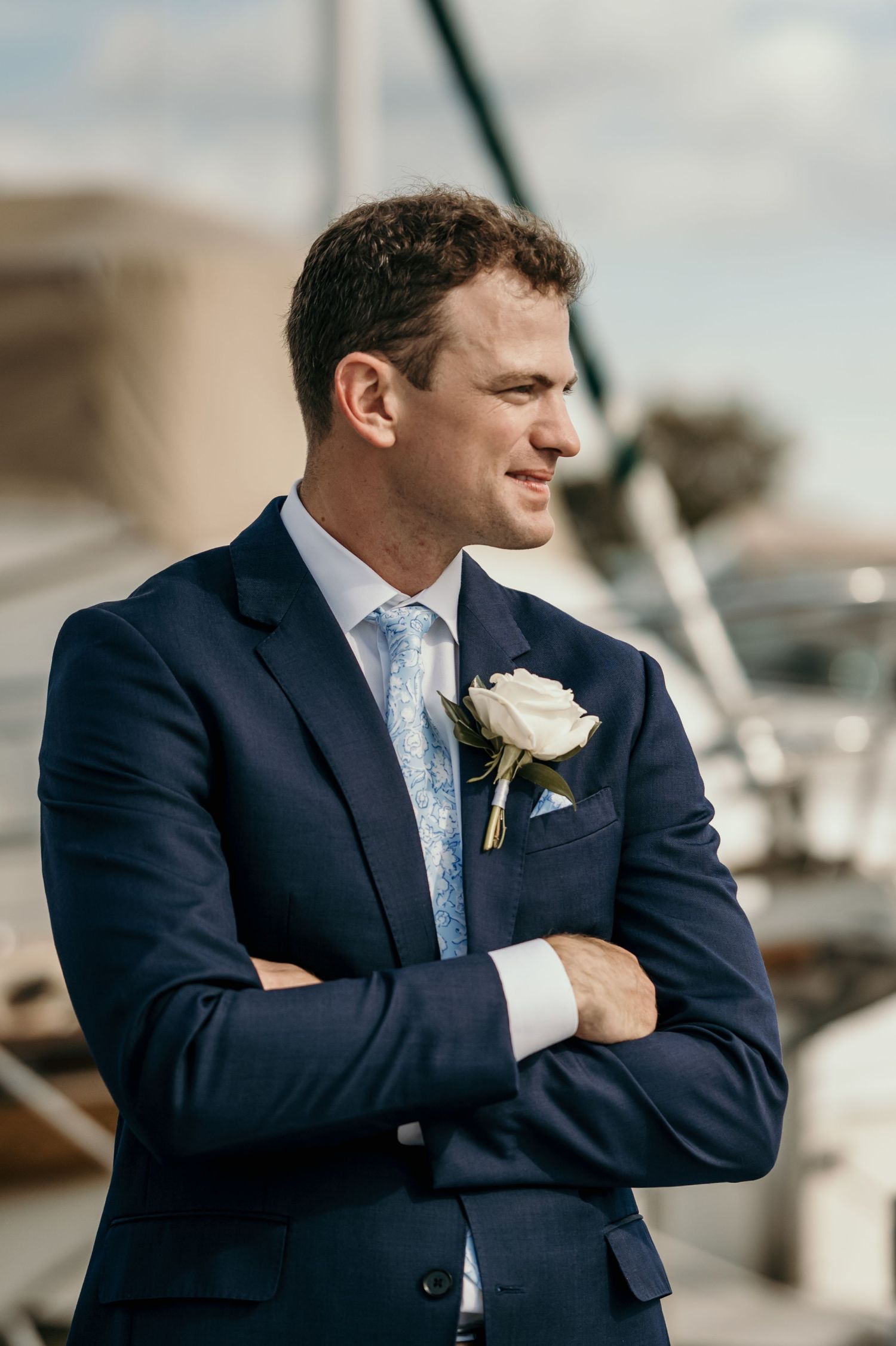 Groom in navy suit with white boutonniere posing at waterfront location.