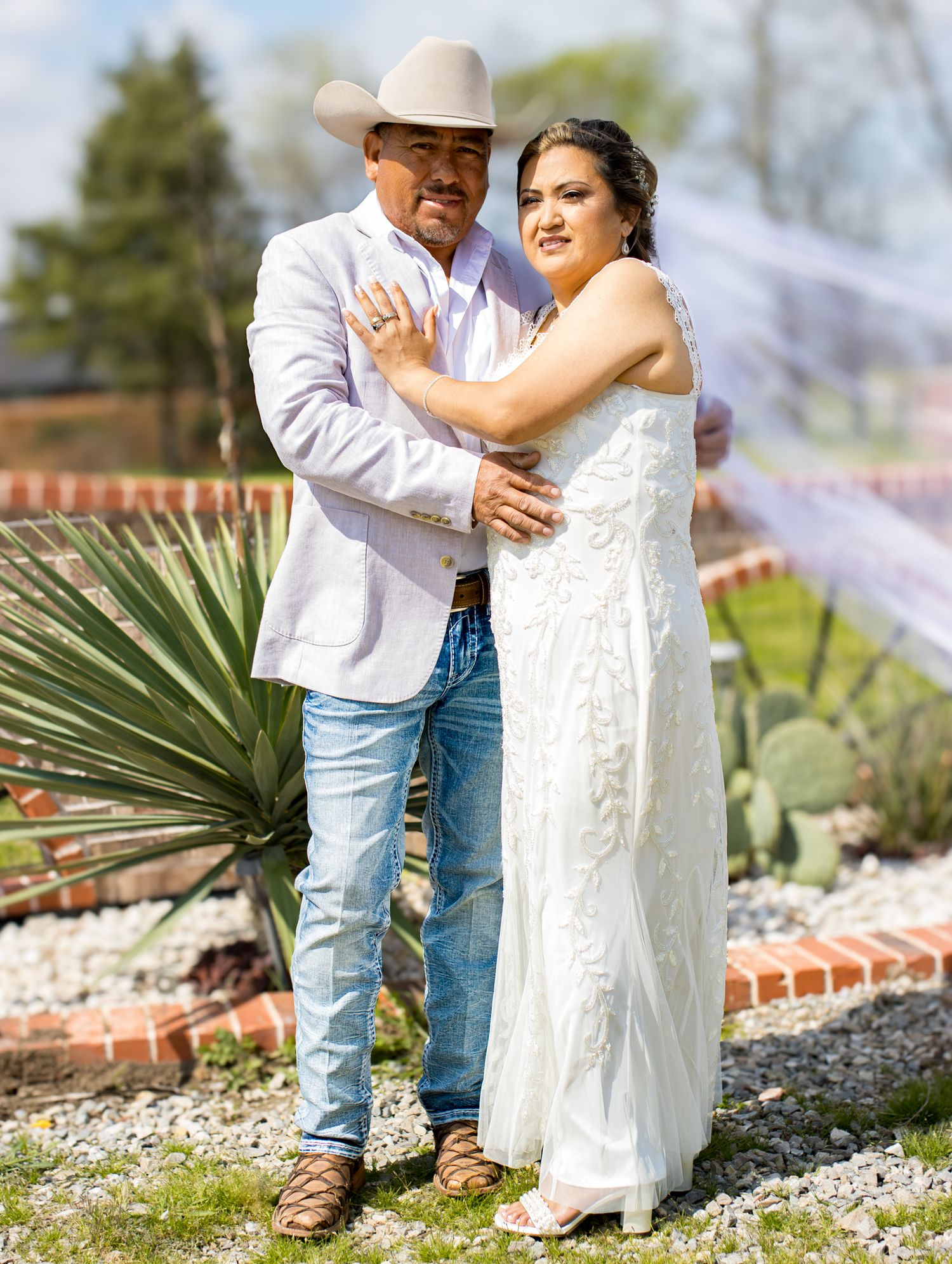 Western-style wedding couple posing in a desert garden with cactus and mountain backdrop.