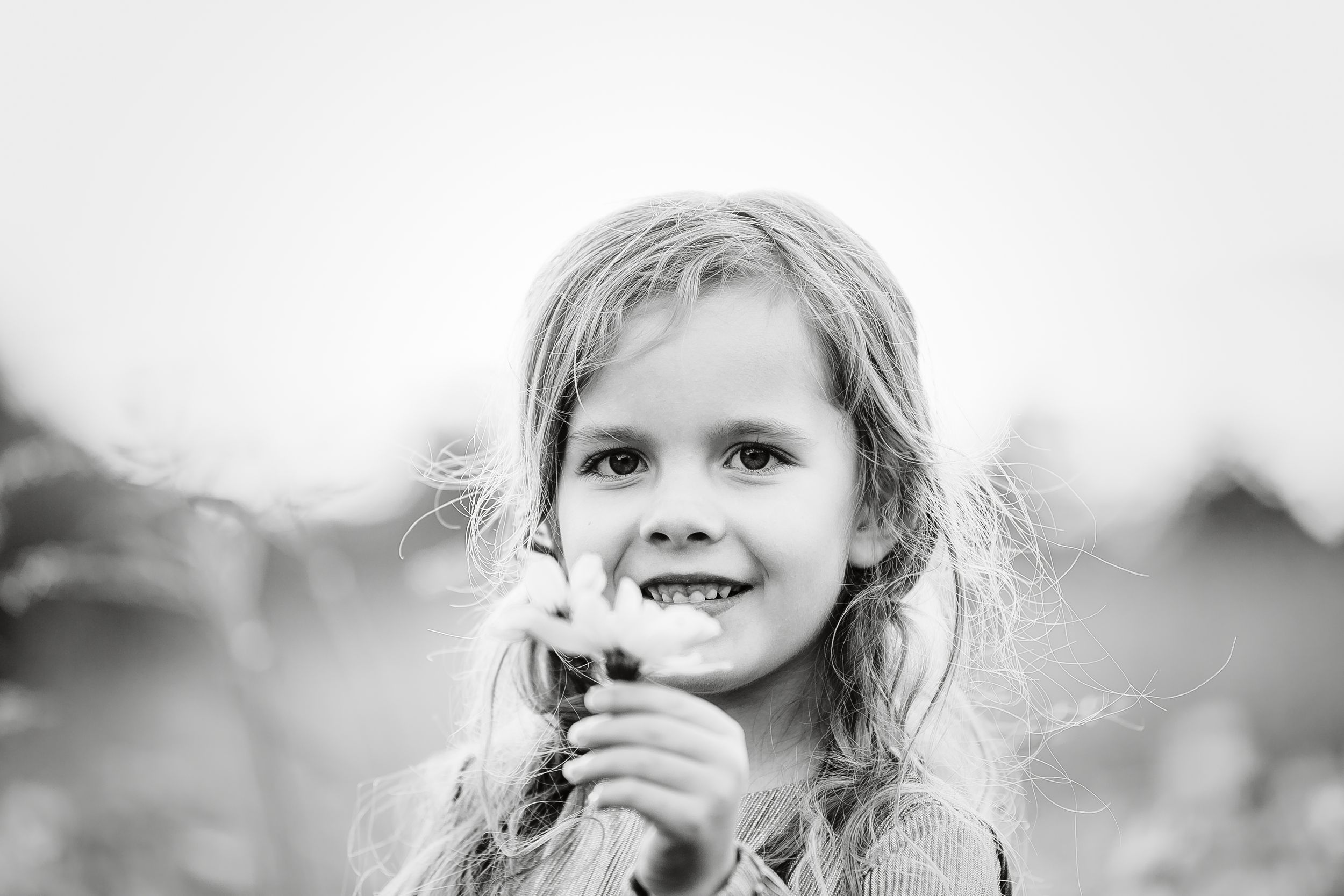 Black and white portrait of a smiling girl holding a flower in a field.