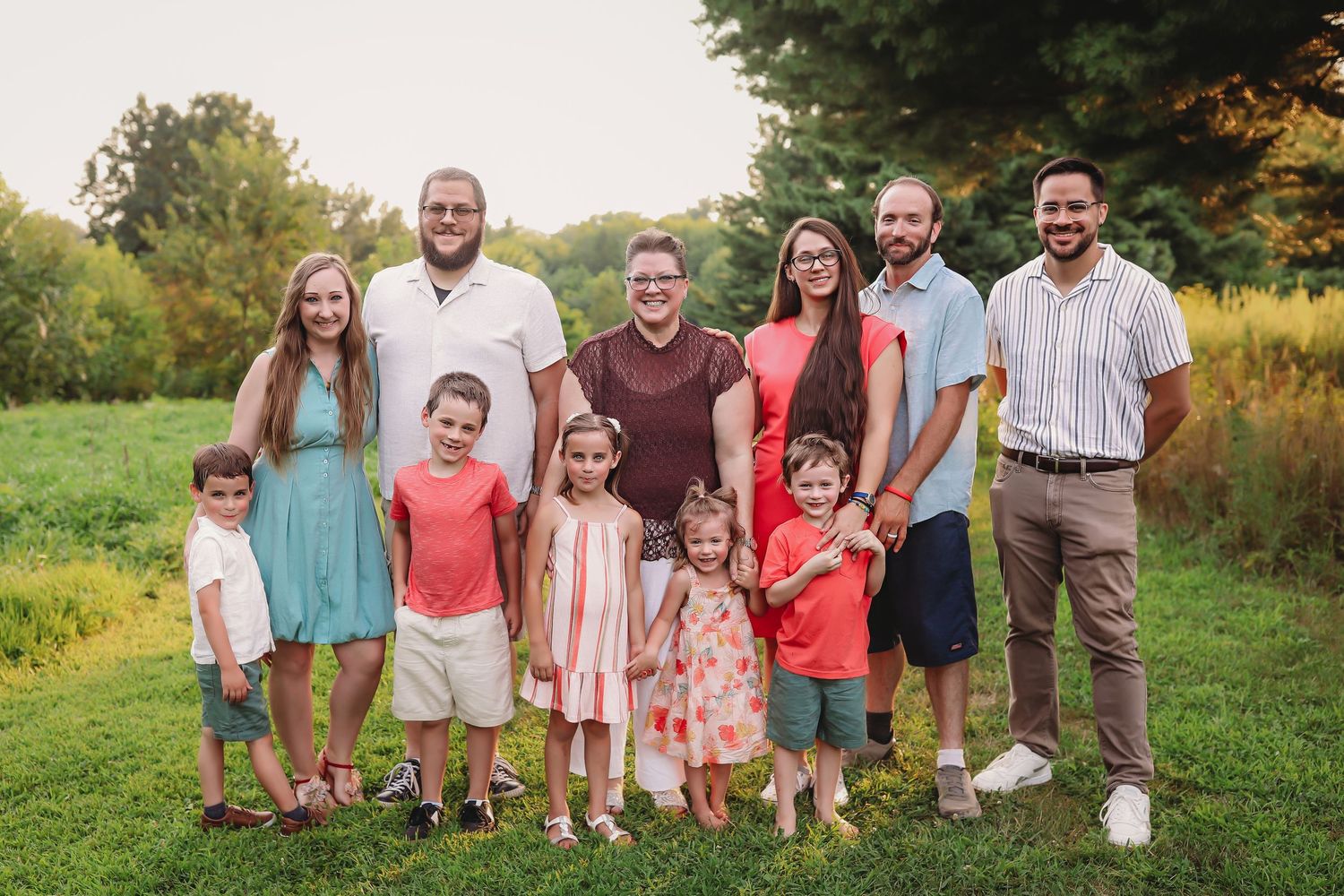 Large family group photo outdoors in a grassy field during golden hour.