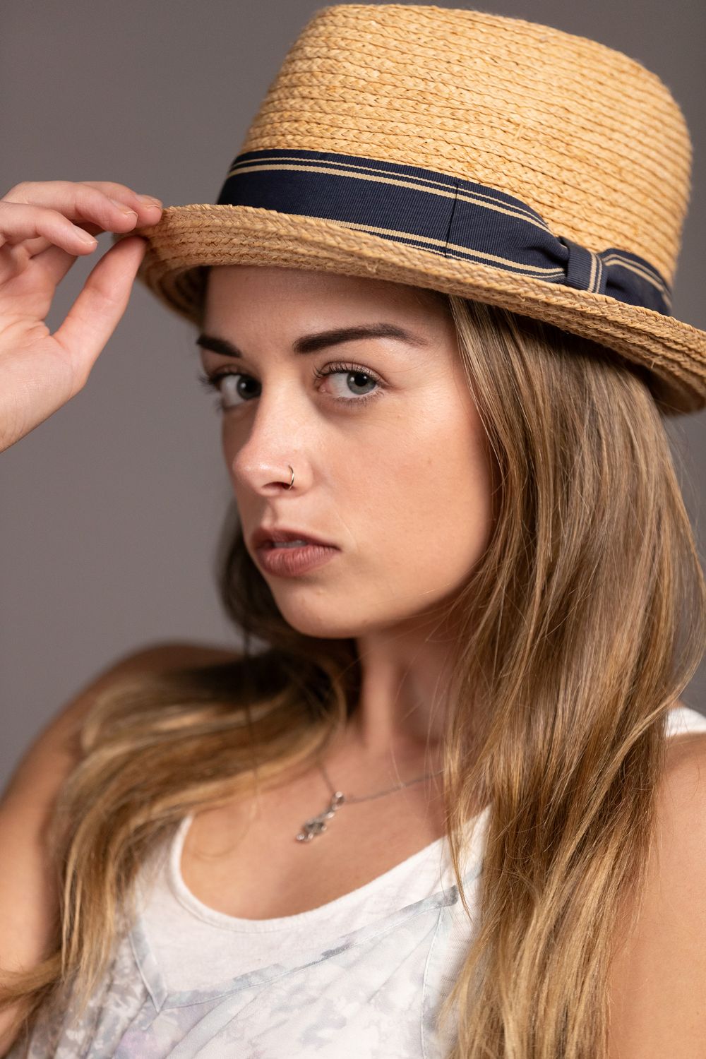 Style portrait featuring a straw fedora hat with navy band against grey background.