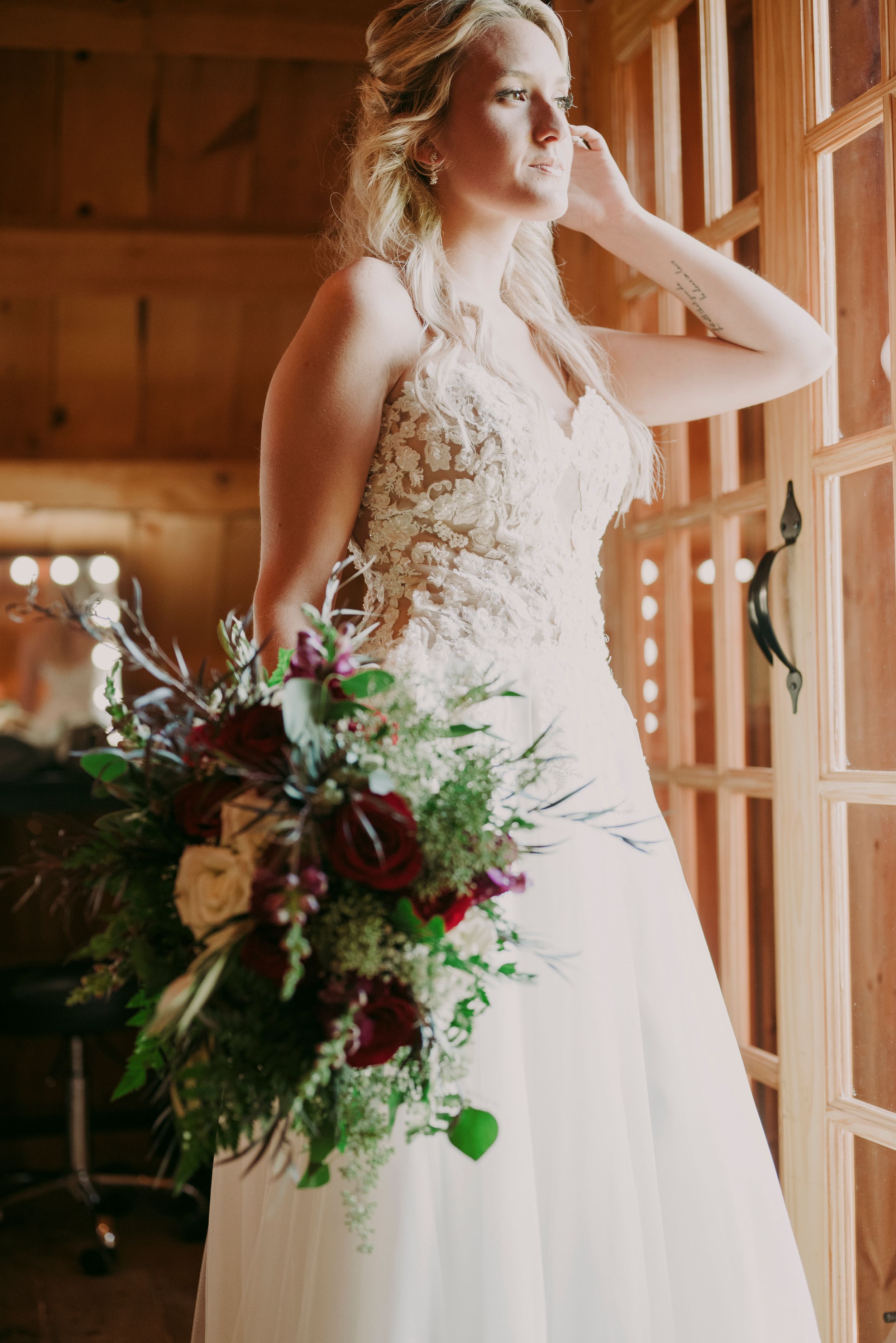 Elegant bride in lace gown holding a lush burgundy and green floral bouquet.