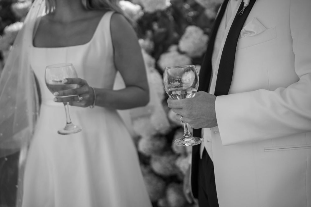 A black and white detail shot of wedding guests holding champagne glasses during a reception.