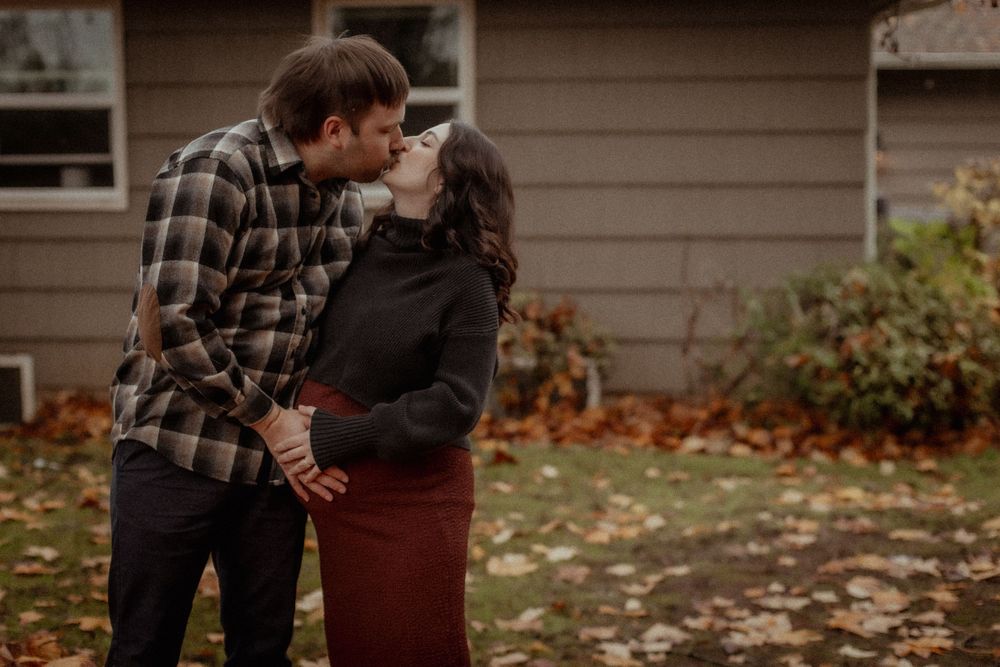 A couple embraces outdoors during autumn with fallen leaves around them. PNW family photographer