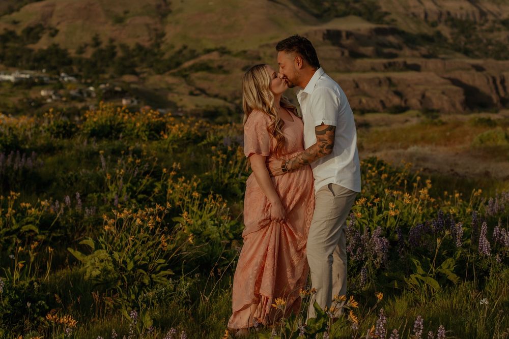 A couple shares a romantic moment among blooming yellow wildflowers during a golden sunset in a hillside meadow.