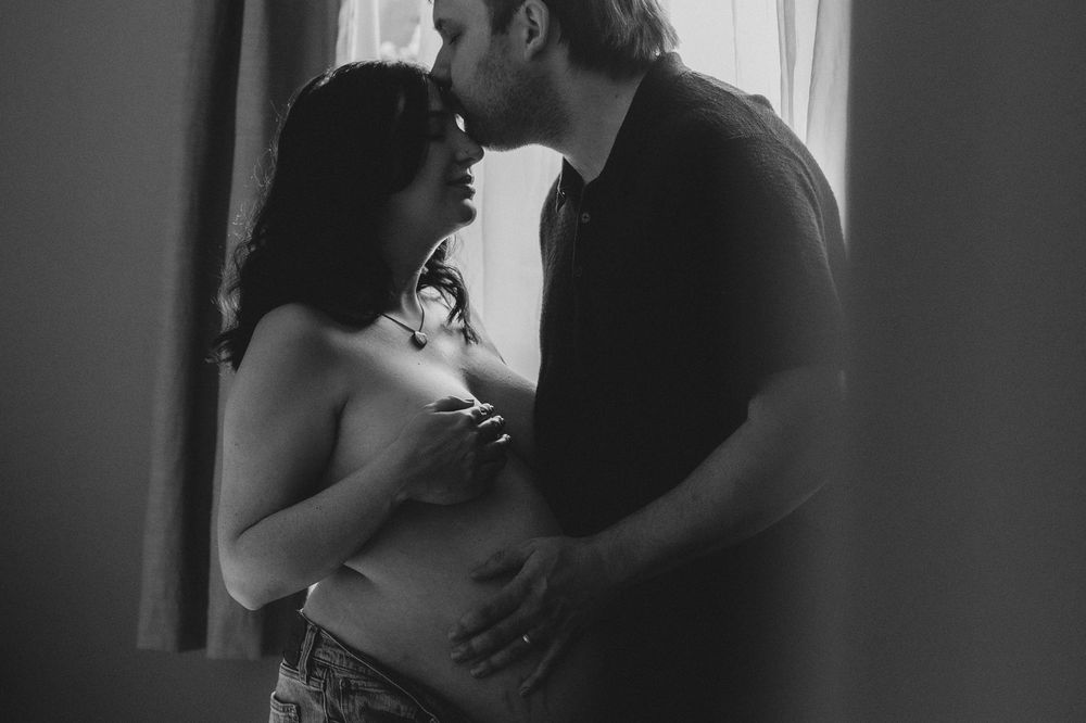 A romantic black and white photo series showing a couple embracing in intimate poses near a window.